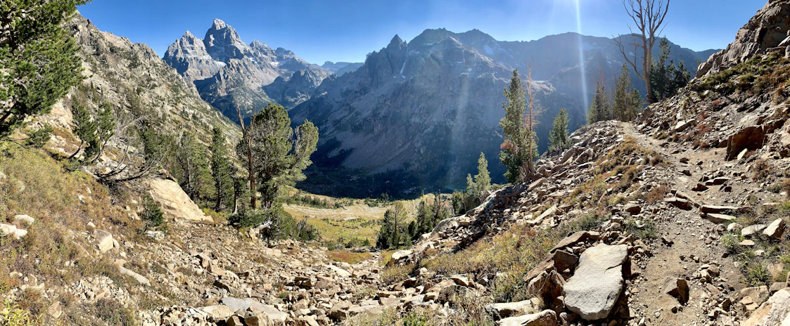 A panoramic view of a rocky trail winding through a sunlit mountain landscape.