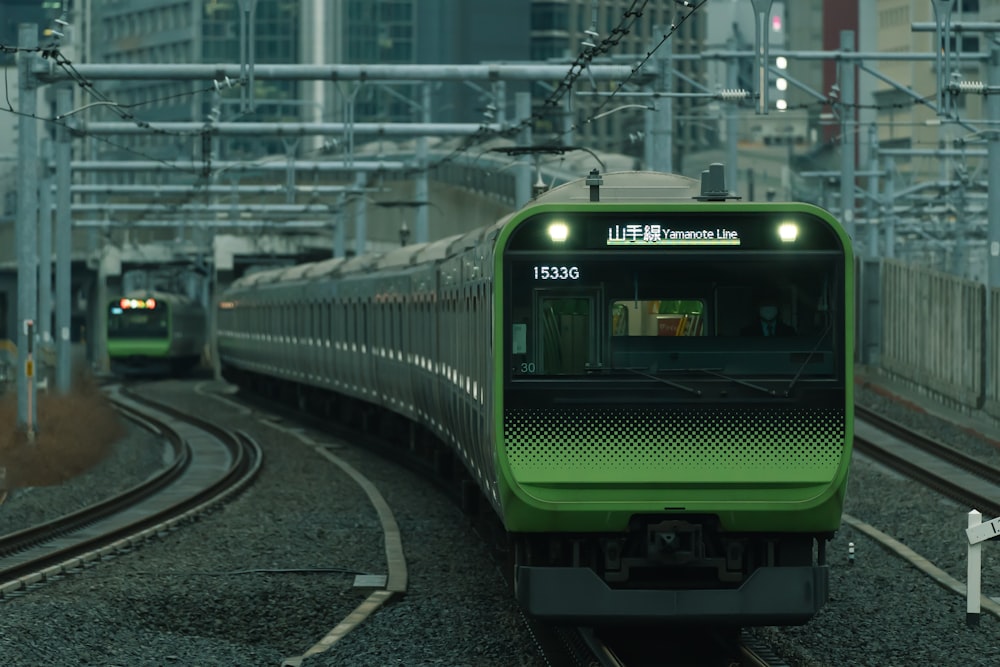 a green train traveling down train tracks next to tall buildings