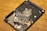 A damaged hard disk drive with broken platters scattered across its surface, showing multiple shards and debris while resting on a wooden surface.