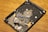 A damaged hard disk drive with broken platters scattered across its surface, showing multiple shards and debris while resting on a wooden surface.