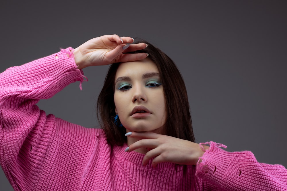 a woman in a pink sweater is holding her hands on her head