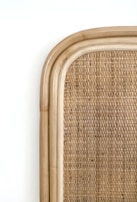 A close-up view of a woven rattan texture framed by a smooth, curved wooden border. The surface displays an intricate pattern of interlaced natural fibers, creating a warm, earthy aesthetic.