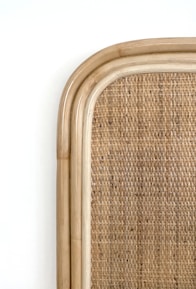 Close-up of textured woven rattan wall decor hanging above a minimalist wooden shelf.