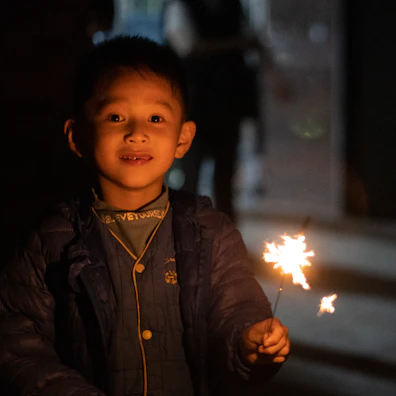 Close-up of a lit sparkler held by a child with a joyful expression.