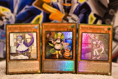 Three Yu-Gi-Oh! trading cards are displayed on a surface. Each card features a character themed as a 'Dragonmaid' with vivid colors and detailed artwork. The cards are titled 'Laundry Dragonmaid', 'Parlor Dragonmaid', and 'Nurse Dragonmaid'. The background has a colorful and abstract design, adding a fantastical atmosphere.
