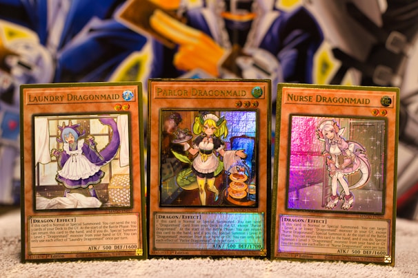 Three Yu-Gi-Oh! trading cards are displayed on a surface. Each card features a character themed as a 'Dragonmaid' with vivid colors and detailed artwork. The cards are titled 'Laundry Dragonmaid', 'Parlor Dragonmaid', and 'Nurse Dragonmaid'. The background has a colorful and abstract design, adding a fantastical atmosphere.