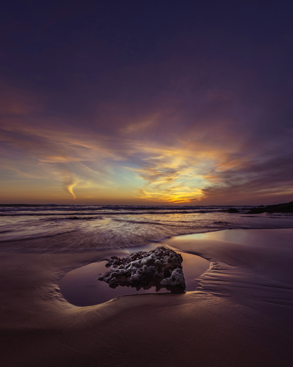 the sun is setting over the ocean with a rock in the foreground