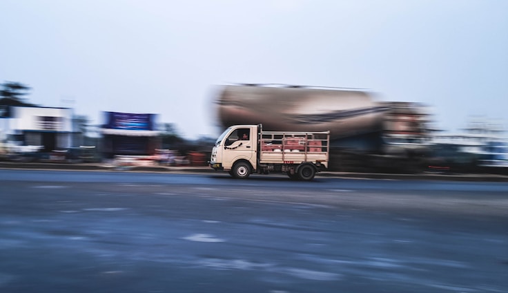 A sleek delivery truck speeding along a highway with motion blur, set against a bright red and silver background.