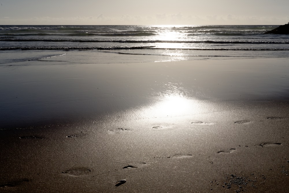 a beach with footprints in the sand and the sun in the background