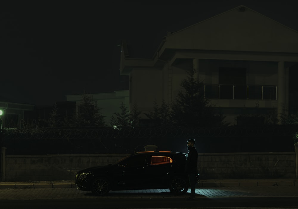 夜に駐車した車の隣に立っている男