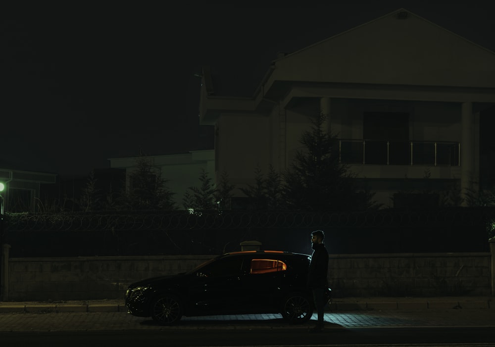 a man standing next to a parked car at night