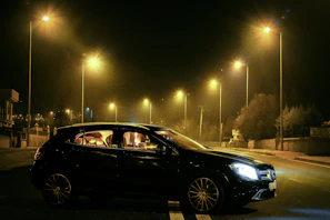 A sleek black sedan parked under soft golden streetlights at night.