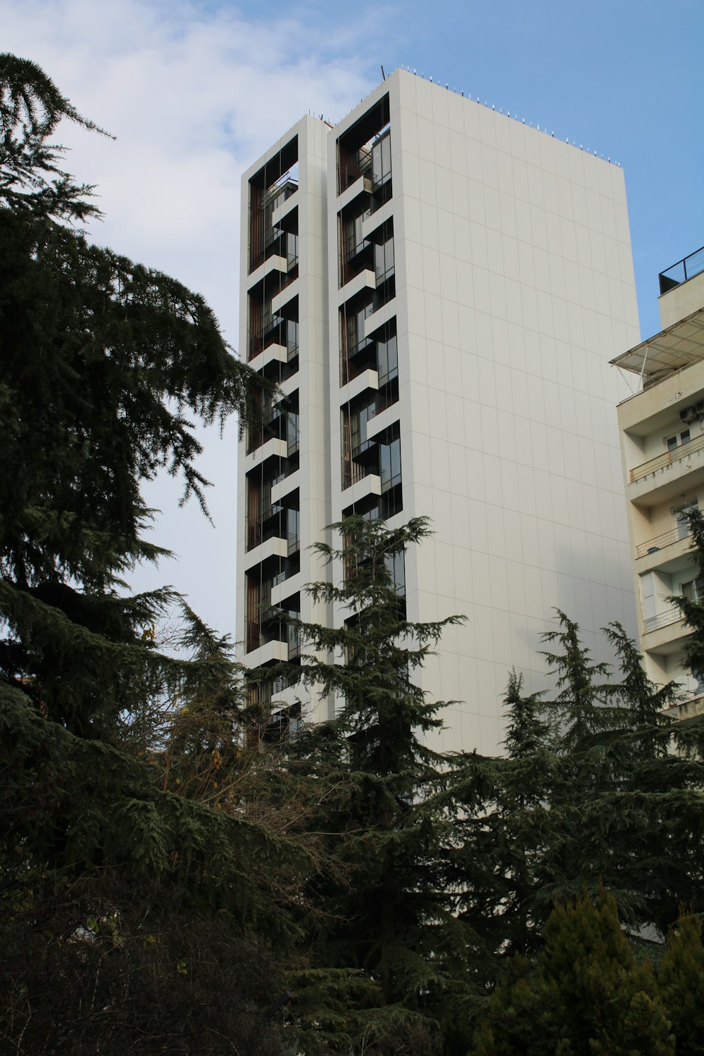 a tall white building sitting next to a forest of trees