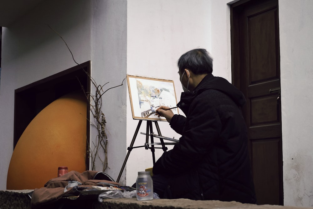 a man sitting in front of a painting on a easel