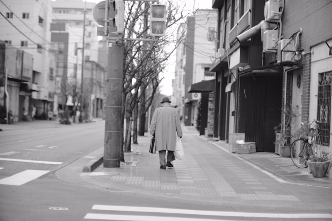 Black and white photograph of a solitary figure walking through a foggy urban street at dawn.