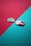 Two guitar picks rest on a surface divided diagonally by contrasting colors, one teal and the other a deep red hue. The picks lie on opposite colors, with one pick a light green, featuring a textured pattern, and the other pink, with a smoother finish.
