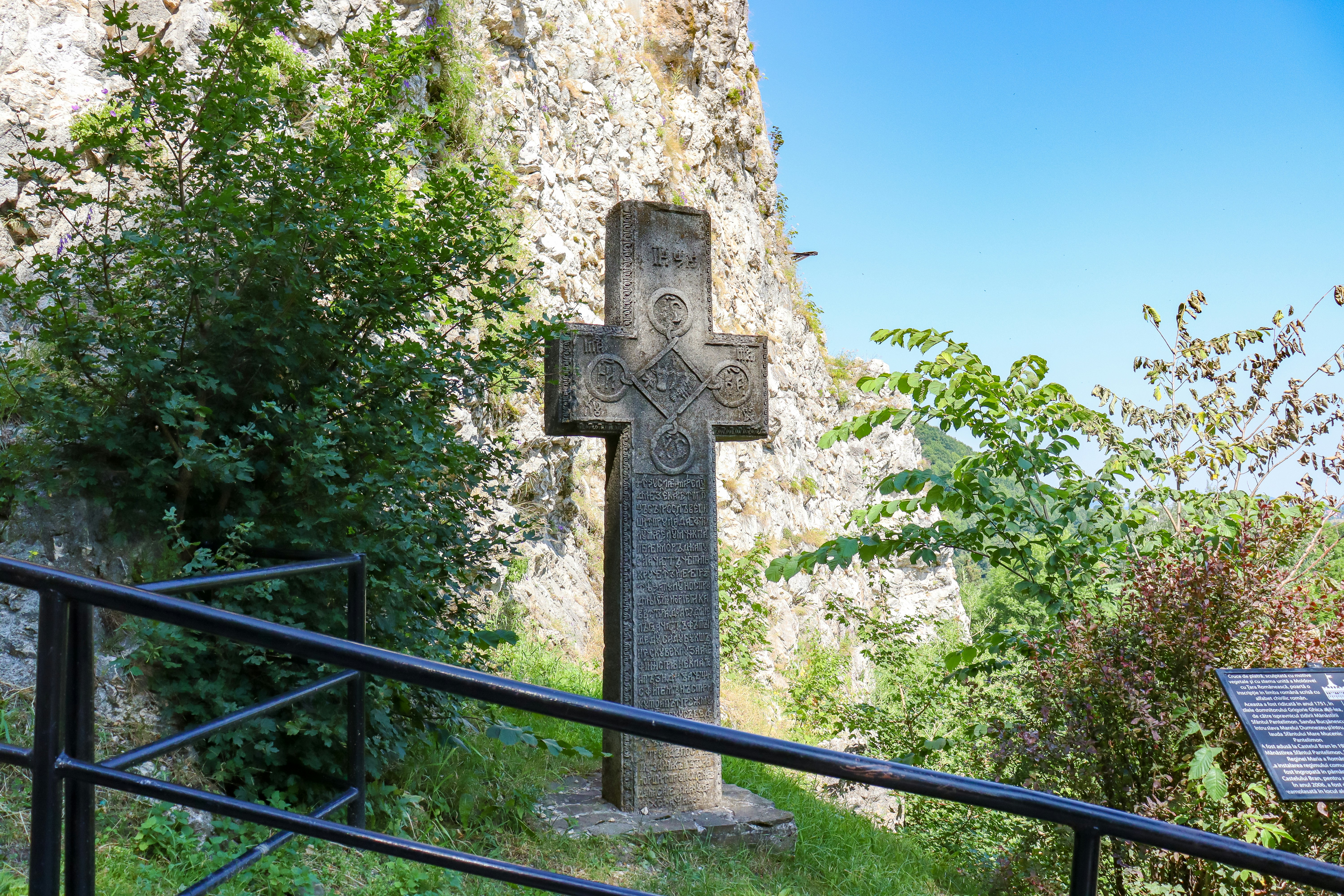 a stone cross in a grassy area next to a cliff