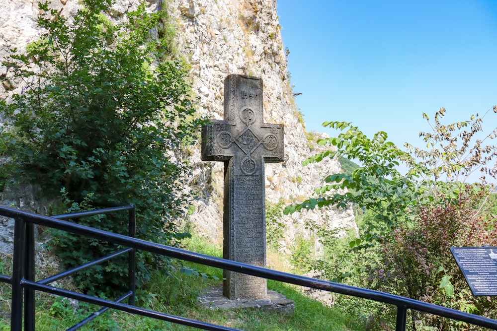 a stone cross in a grassy area next to a cliff