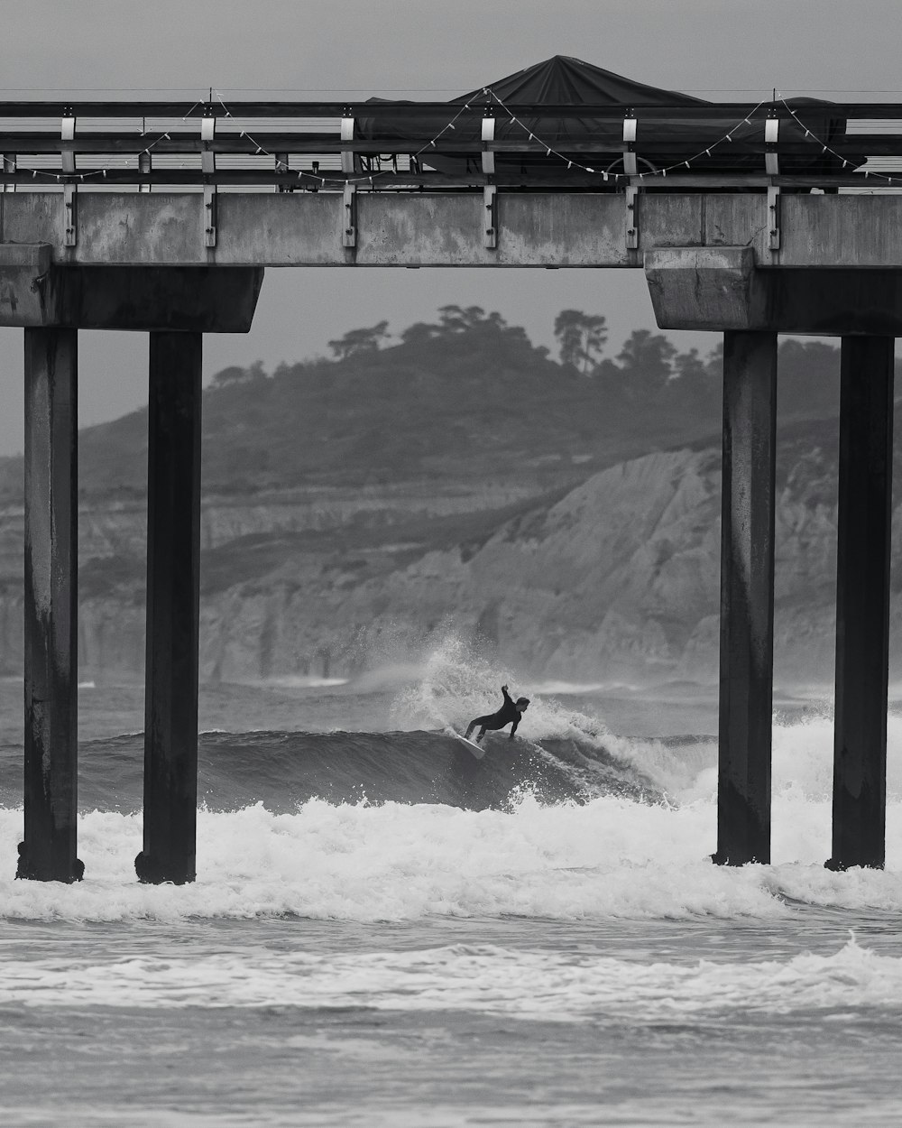 a surfer riding a wave under a bridge