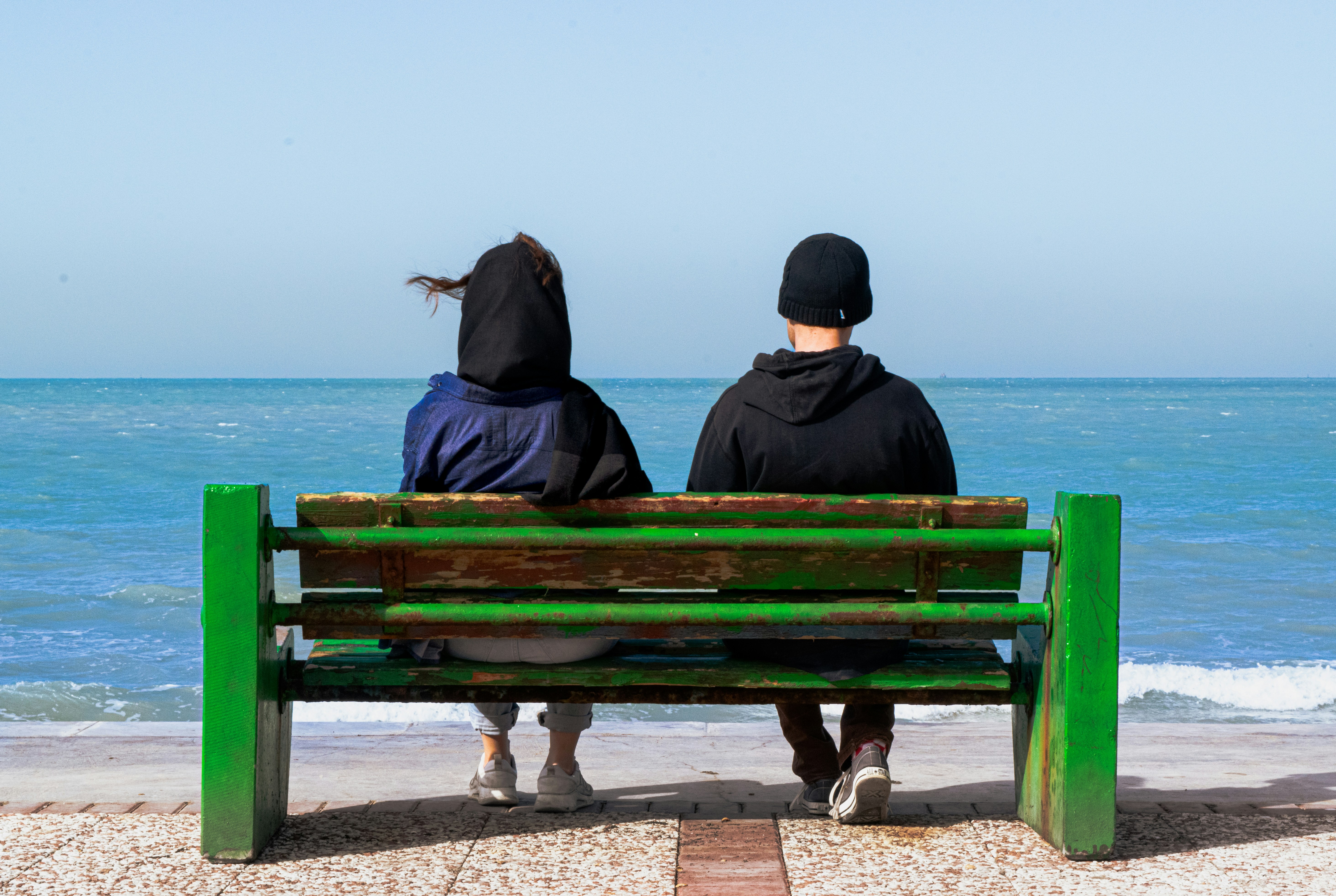 two people sitting on a bench looking out at the ocean, 