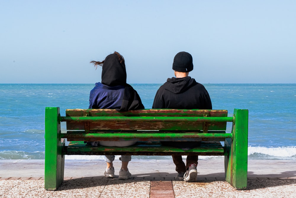 two people sitting on a bench looking out at the ocean