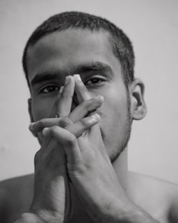 A person appears contemplative, with their hands clasped and raised towards their face. The monochromatic image highlights their short hair and focused expression.