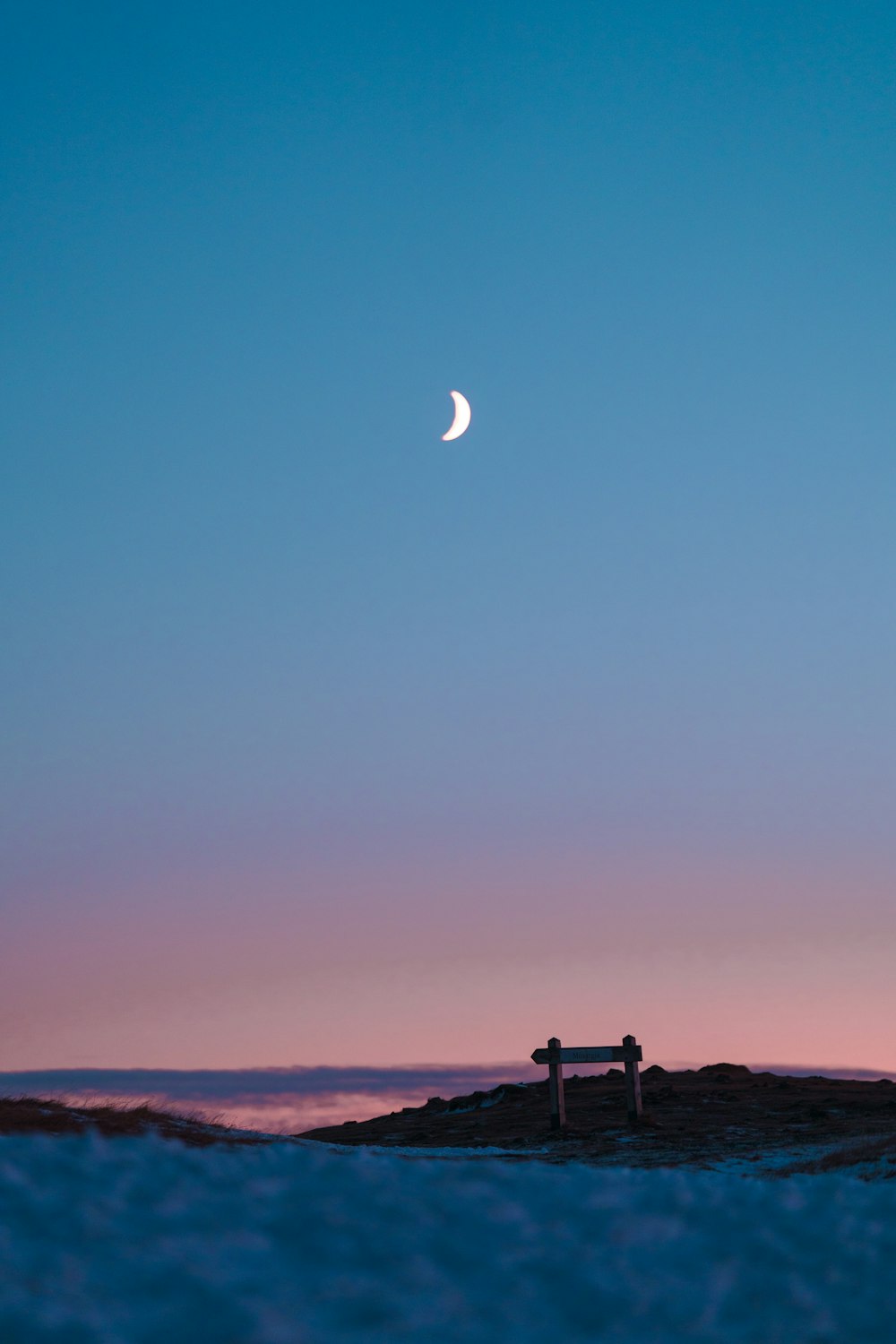 Un banco sentado en la cima de una playa de arena bajo una luna