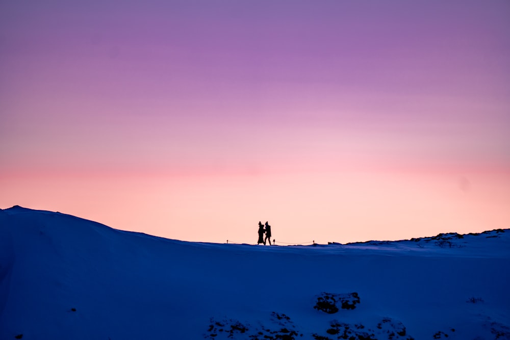 a couple of people standing on top of a snow covered slope