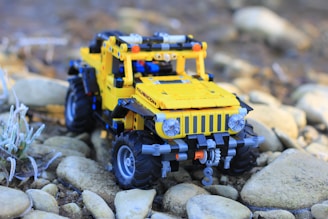 A detailed model of a yellow LEGO jeep is placed on a rocky surface. The toy jeep features realistic details, including headlights, a visible grille, and rugged tires designed for off-road exploration.
