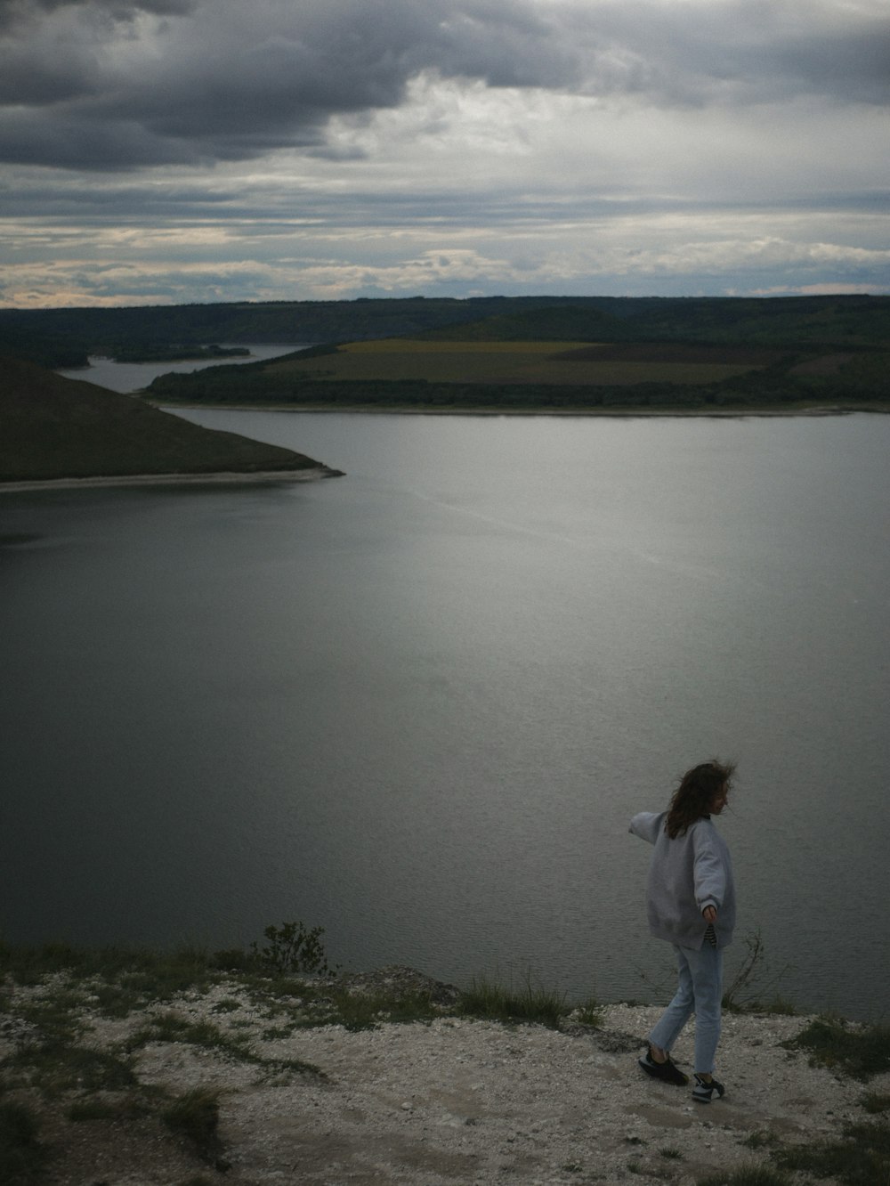 a woman standing on top of a hill next to a lake