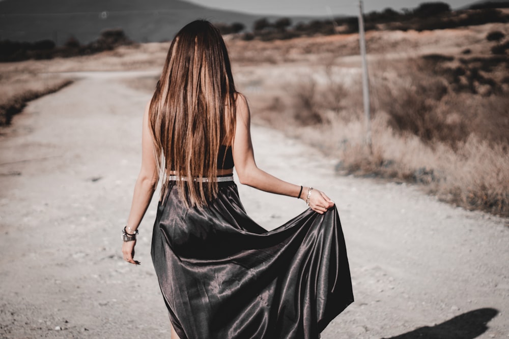 a woman in a black dress walking down a dirt road