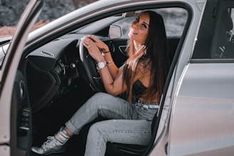 A smiling driver opening the car door for a happy passenger in an urban setting.