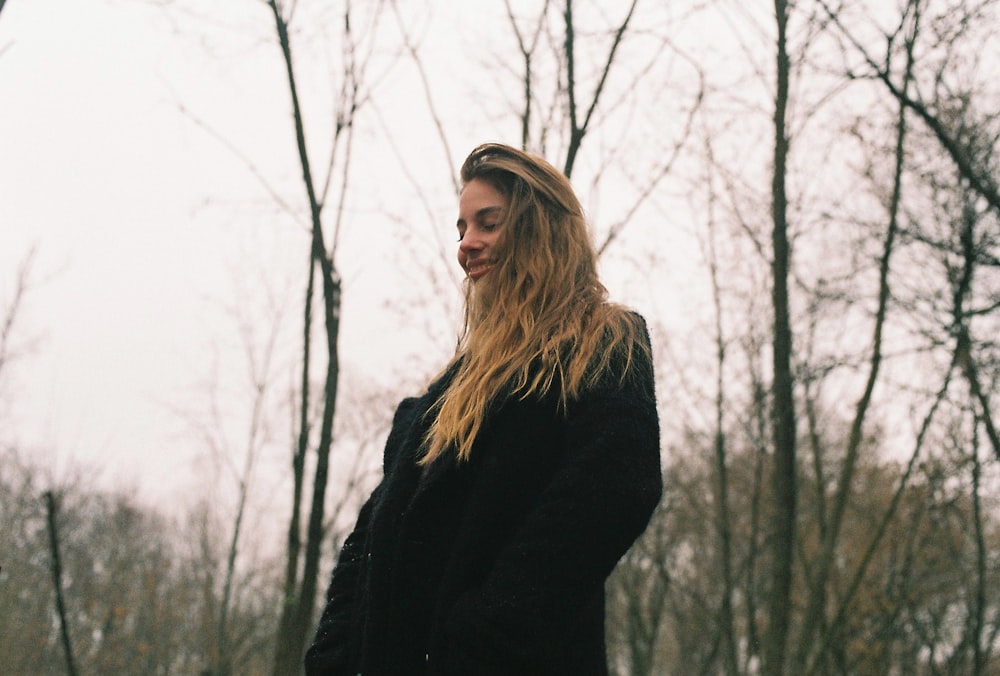 a woman standing in the woods with her hair blowing in the wind