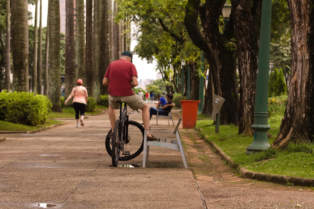 a man riding a bike down a sidewalk next to a park bench