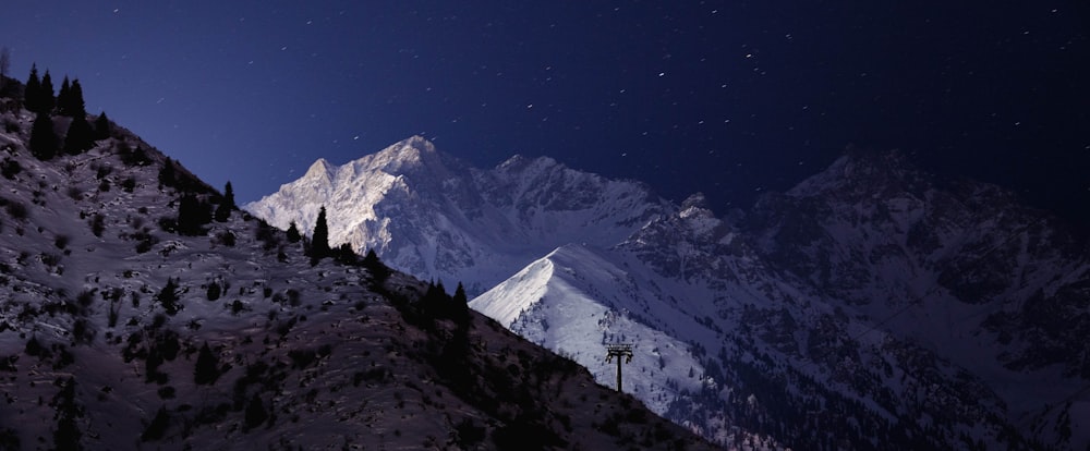 a night view of a snowy mountain with a telephone pole in the foreground