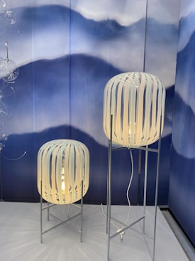 Two standing lamps with white striped shades on metal stands, set against a backdrop of artistic blue and white waves. The design is modern and artistic, giving a stylish aesthetic.