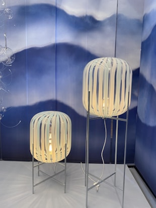 Two standing lamps with white striped shades on metal stands, set against a backdrop of artistic blue and white waves. The design is modern and artistic, giving a stylish aesthetic.