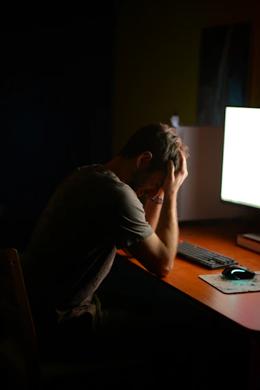 A frustrated business owner staring at a slow, cluttered computer screen in a dimly lit office.