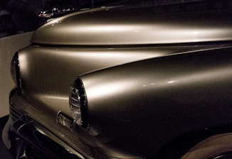 Close-up of a craftsman polishing a gleaming vintage car hood under soft lighting.