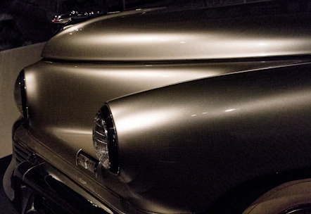 Close-up of a craftsman polishing a gleaming vintage car hood under soft lighting.