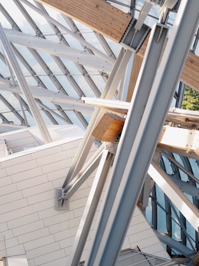 A complex structure featuring intersecting beams and panels made of both metal and wood. The architecture involves large glass panels allowing natural light to filter through, creating a modern and geometric design.
