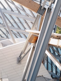 A complex structure featuring intersecting beams and panels made of both metal and wood. The architecture involves large glass panels allowing natural light to filter through, creating a modern and geometric design.