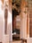 A cozy indoor seating area framed by tall, beige curtains and ornate wooden pillars. The room features a soft, cushioned bench with several accent cushions, and a decorative iron window grate. Sunlight filters into the space, creating a tranquil and inviting atmosphere.