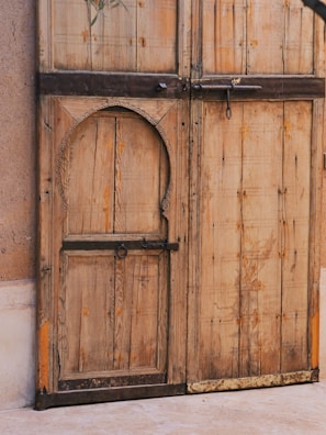 A large, rustic wooden door with intricate carvings and metal accents, featuring a smaller door inset within it. The wood appears weathered, giving it a vintage and historic look.