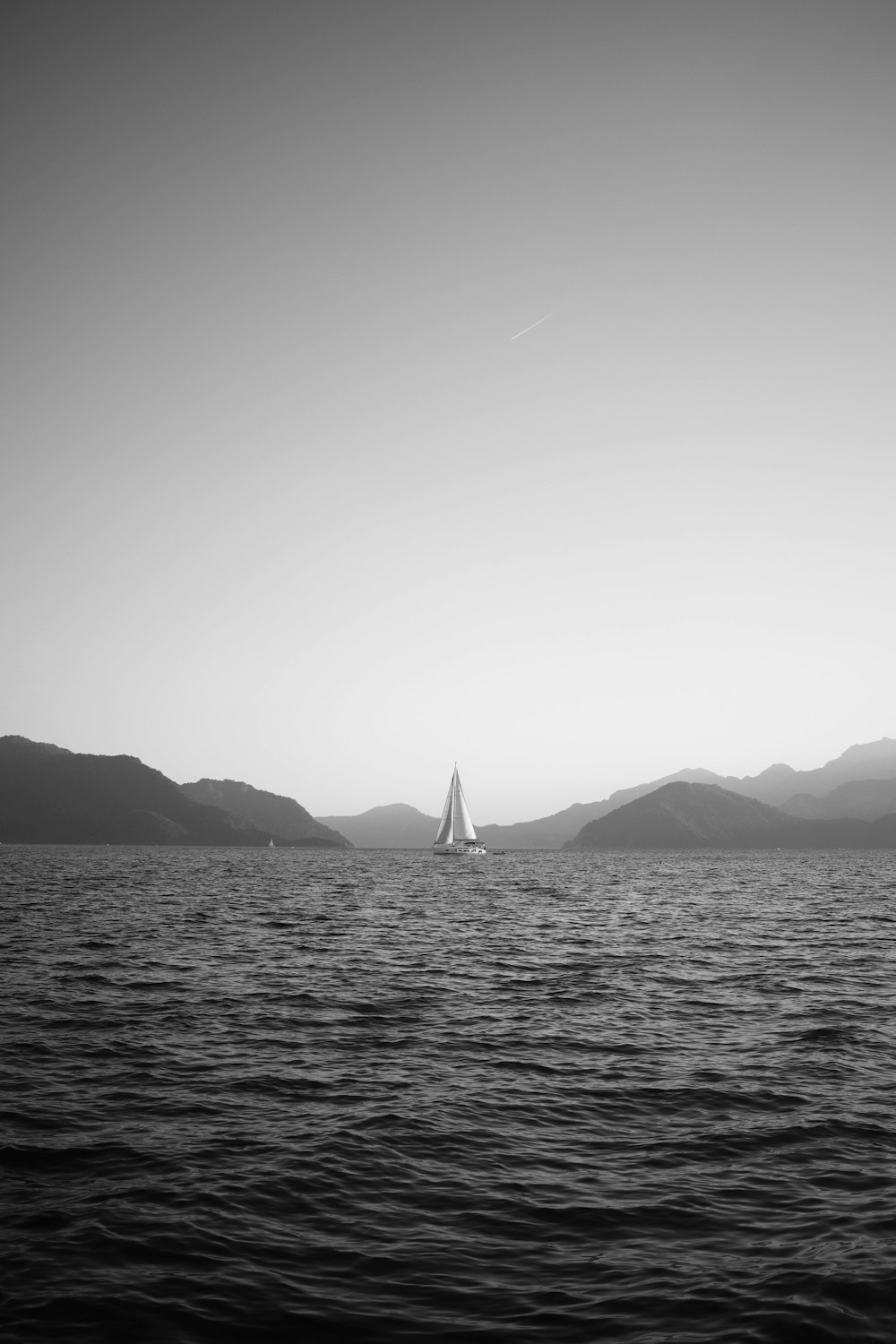 a black and white photo of a sailboat in the ocean