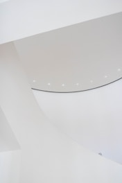 Curved architectural structures with a smooth, white surface create a minimalist aesthetic. Subtle lighting adds a soft glow to the design.