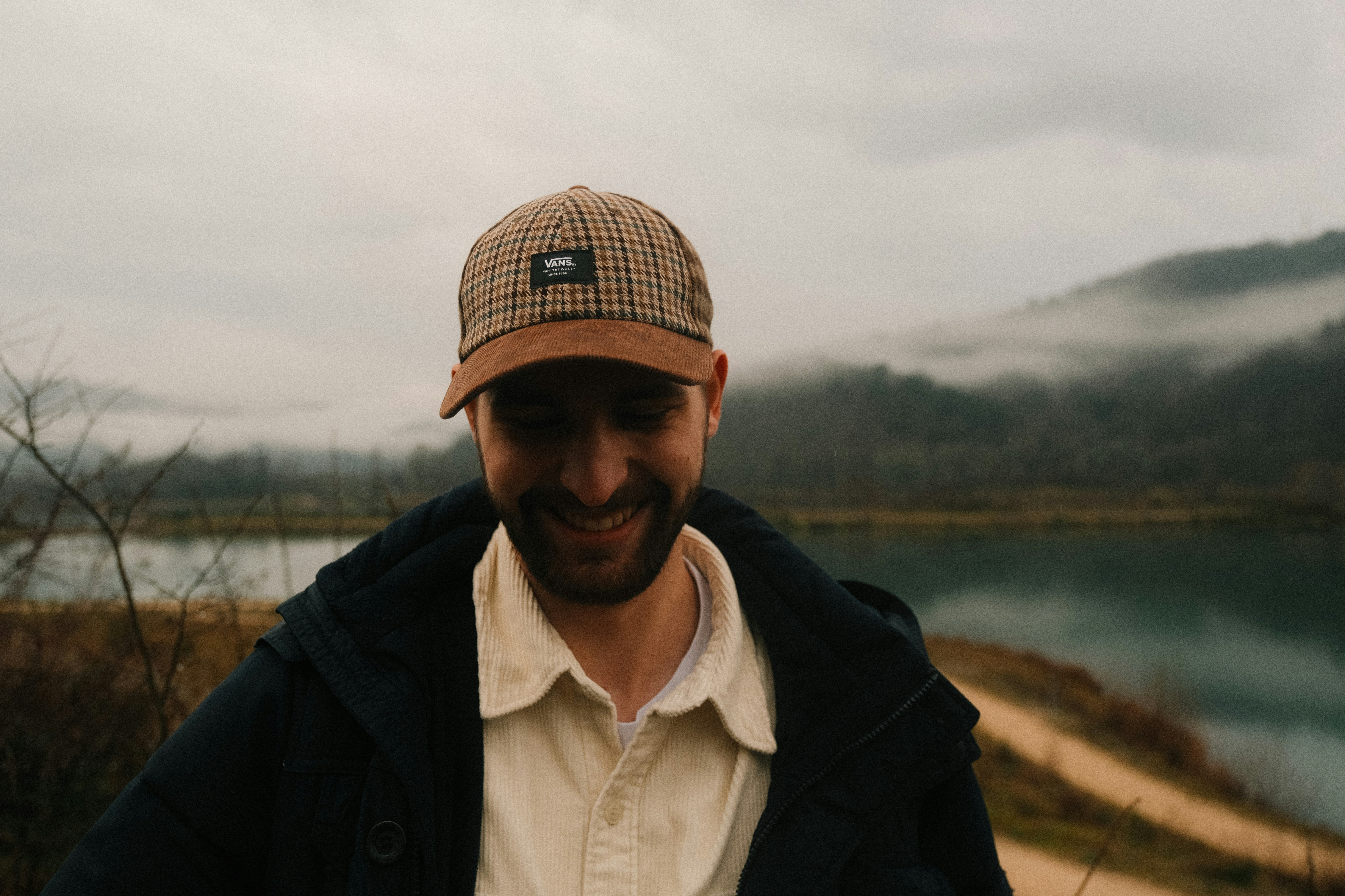a man wearing a hat standing in front of a lake