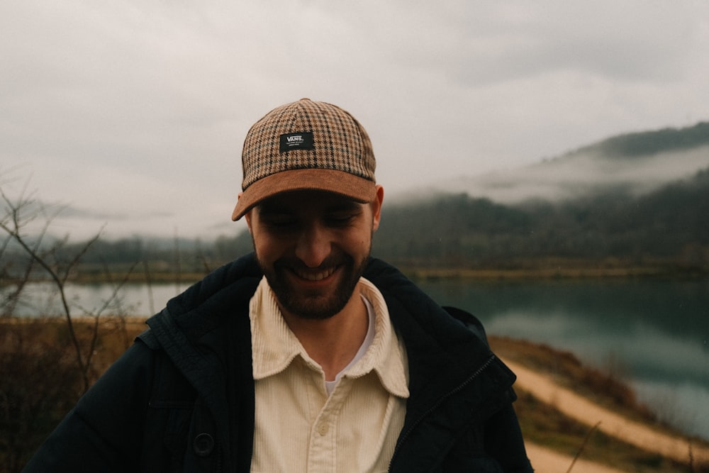 a man wearing a hat standing in front of a lake