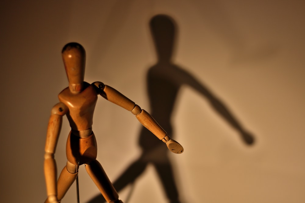 a wooden mannequin casting a shadow on a wall