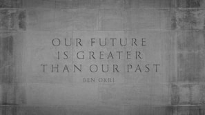 An inspirational quote by Ben Okri is etched onto a stone wall. The quote reads 'Our future is greater than our past' and is set in a serif font. The background is textured stone, giving a sense of permanence and strength.